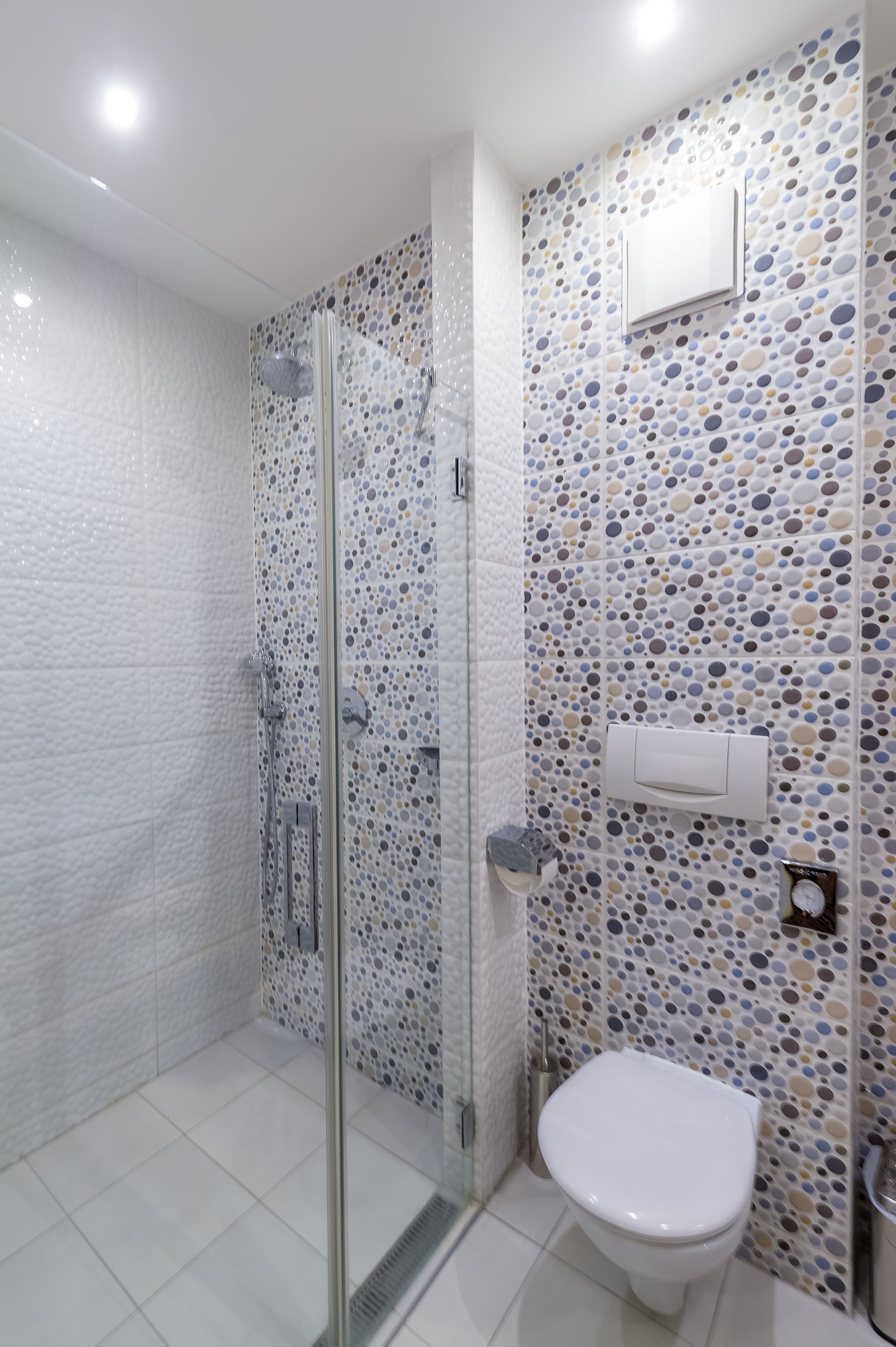A modern bathroom with a glass shower enclosure, a toilet, and a wall with a polka dot tile pattern.