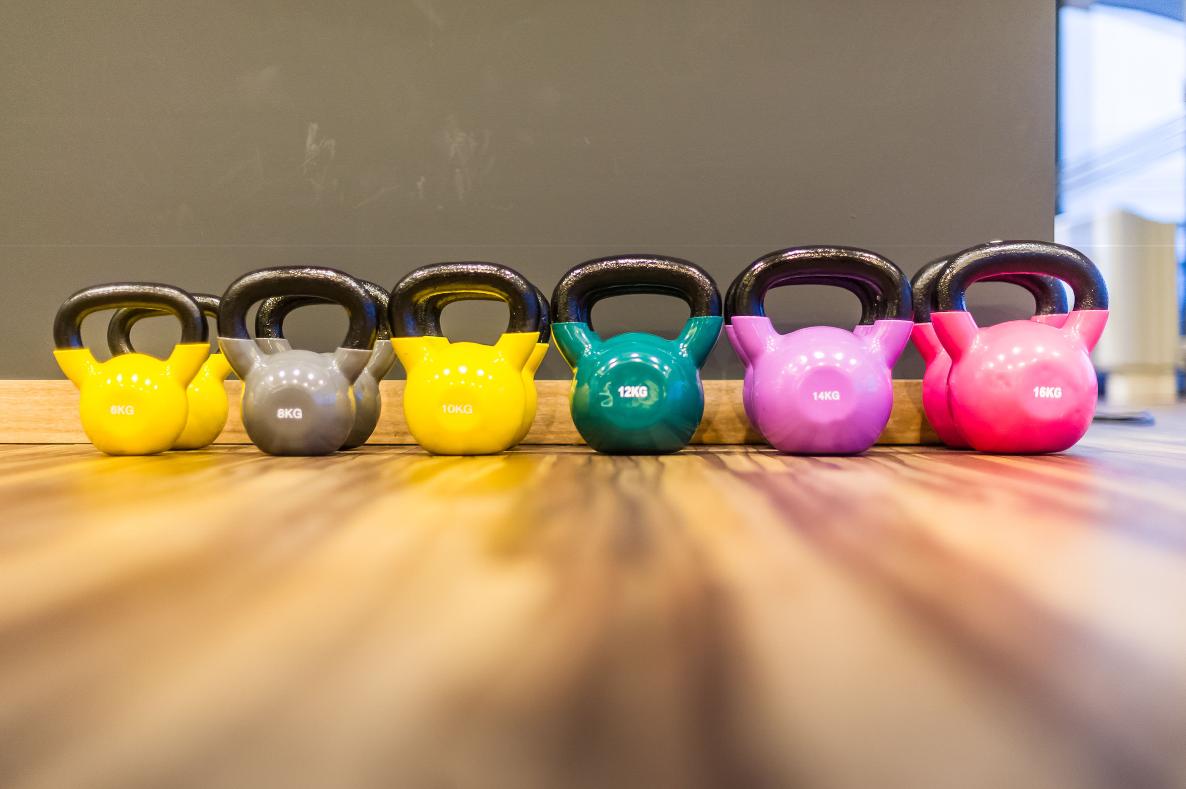 Une rangée de kettlebells aux couleurs vives sur un plancher en bois.