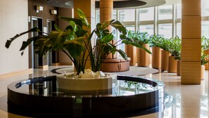 A modern lobby with a central circular water feature, potted plants, and a seating area. - Aquaticum Debrecen Thermal and Wellness Hotel (Debrecen)