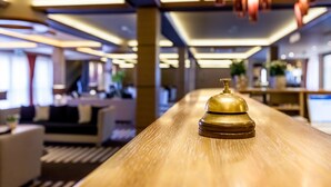 A hotel reception desk with a golden bell, modern lighting, and a blurred background suggesting a spacious interior. - Aquaticum Debrecen Thermal and Wellness Hotel (Debrecen)