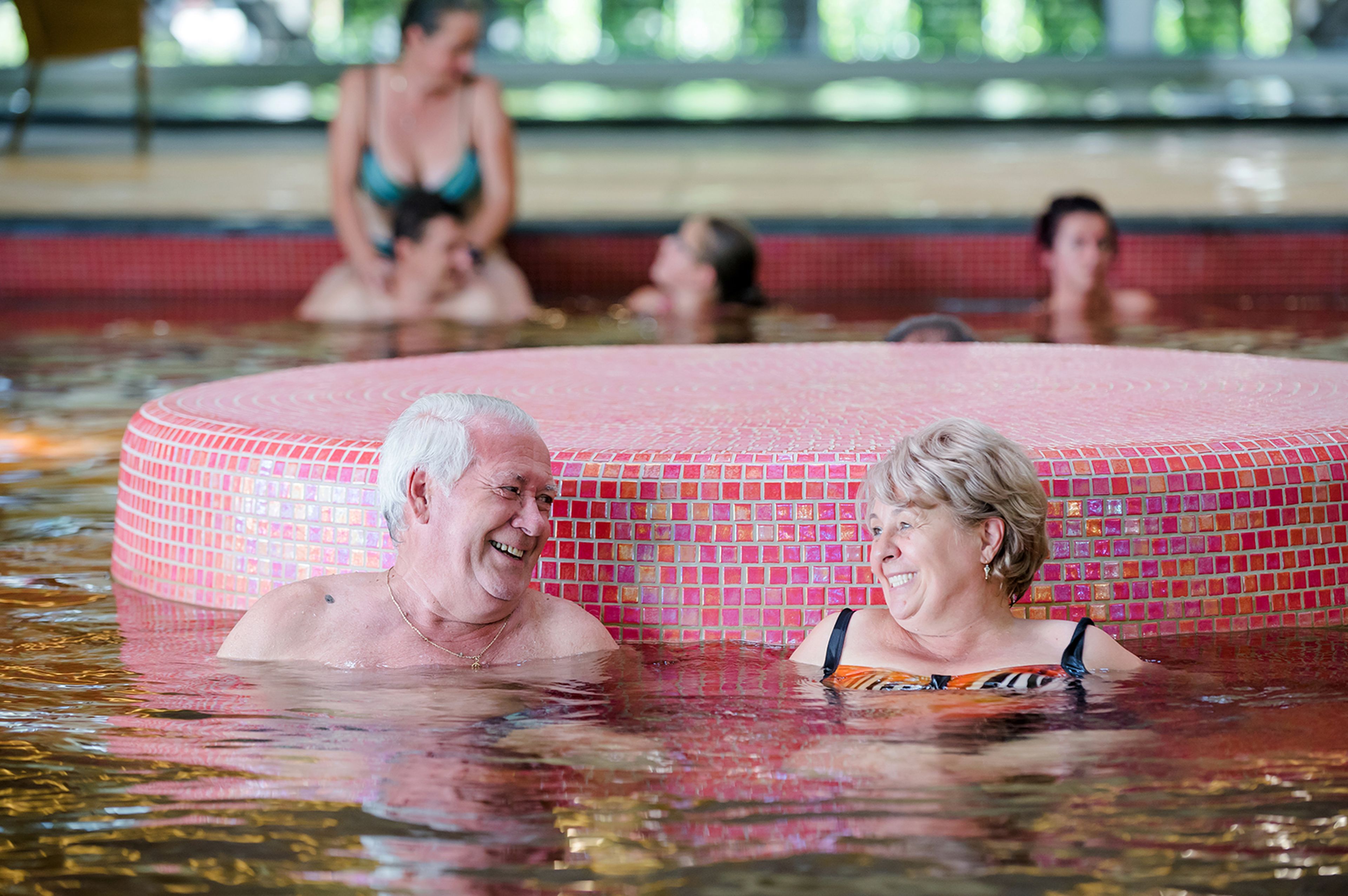 A pool area with a tiled hot tub and people swimming.