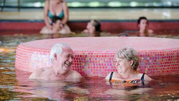 A pool area with a tiled hot tub and people swimming.