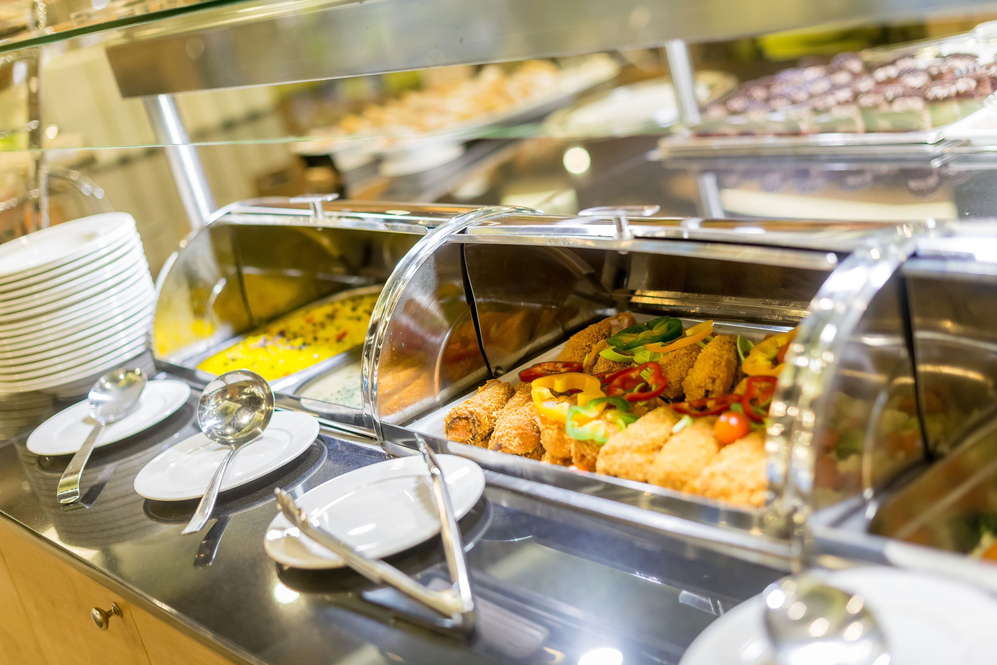 A buffet with various food items, including fried foods and salads, and serving utensils like plates and spoons.