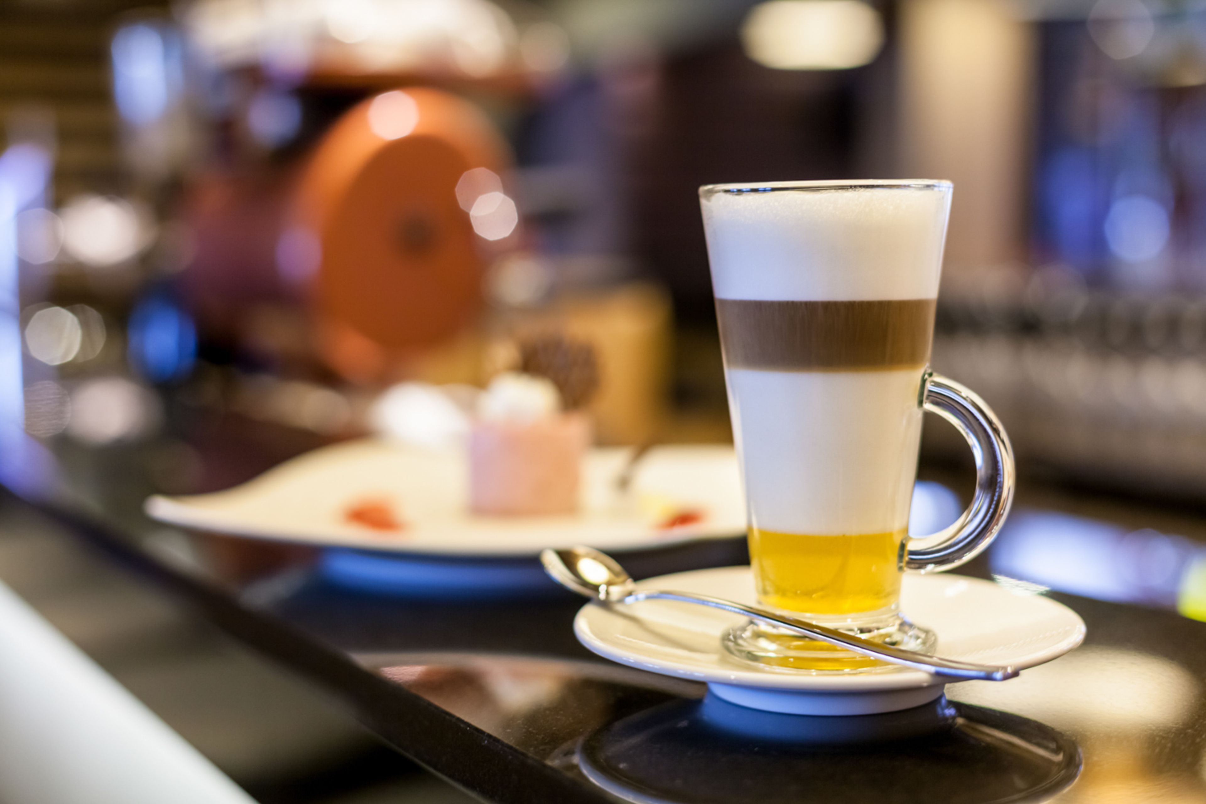 A glass of beer on a coaster with a spoon, on a bar counter.