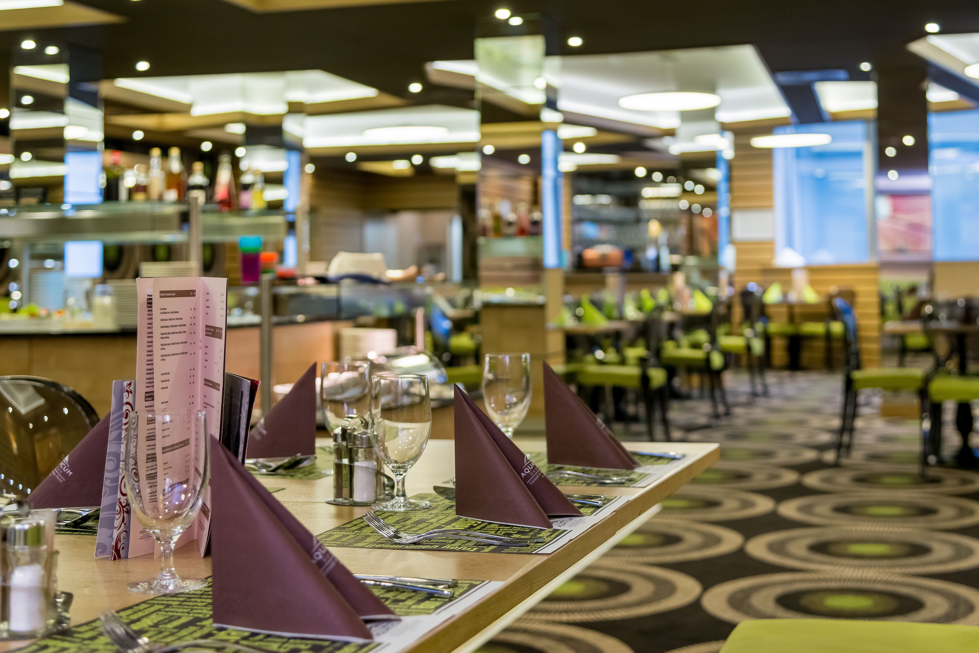 A restaurant setting with a long table set with menus, wine glasses, and cutlery.