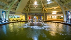 A large indoor pool with a central fountain, surrounded by lounge chairs and a reception area with plants. - Aquaticum Debrecen Thermal and Wellness Hotel (Debrecen)