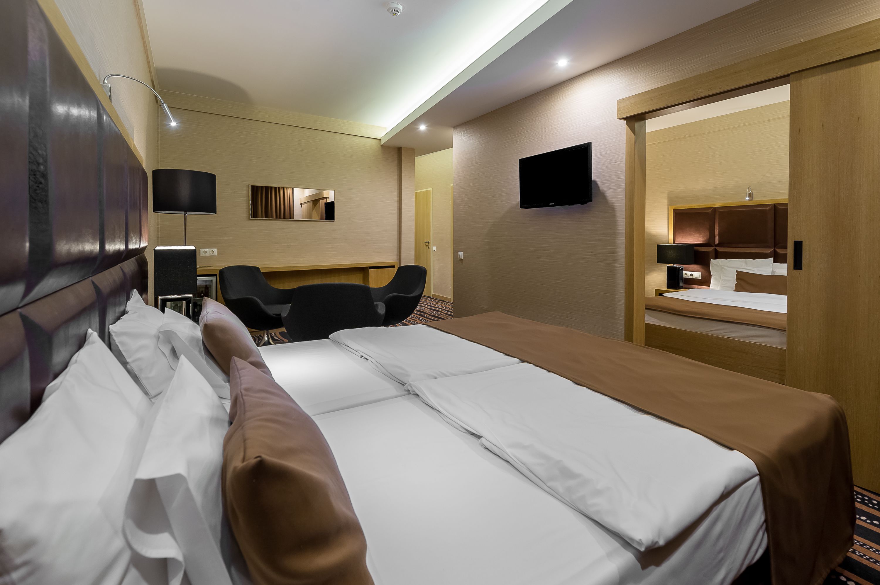Ein Hotelzimmer mit einem großen Bett, einem Schreibtisch mit Stuhl, einem flachbildfernseher an der Wand und einem Holzschrank.