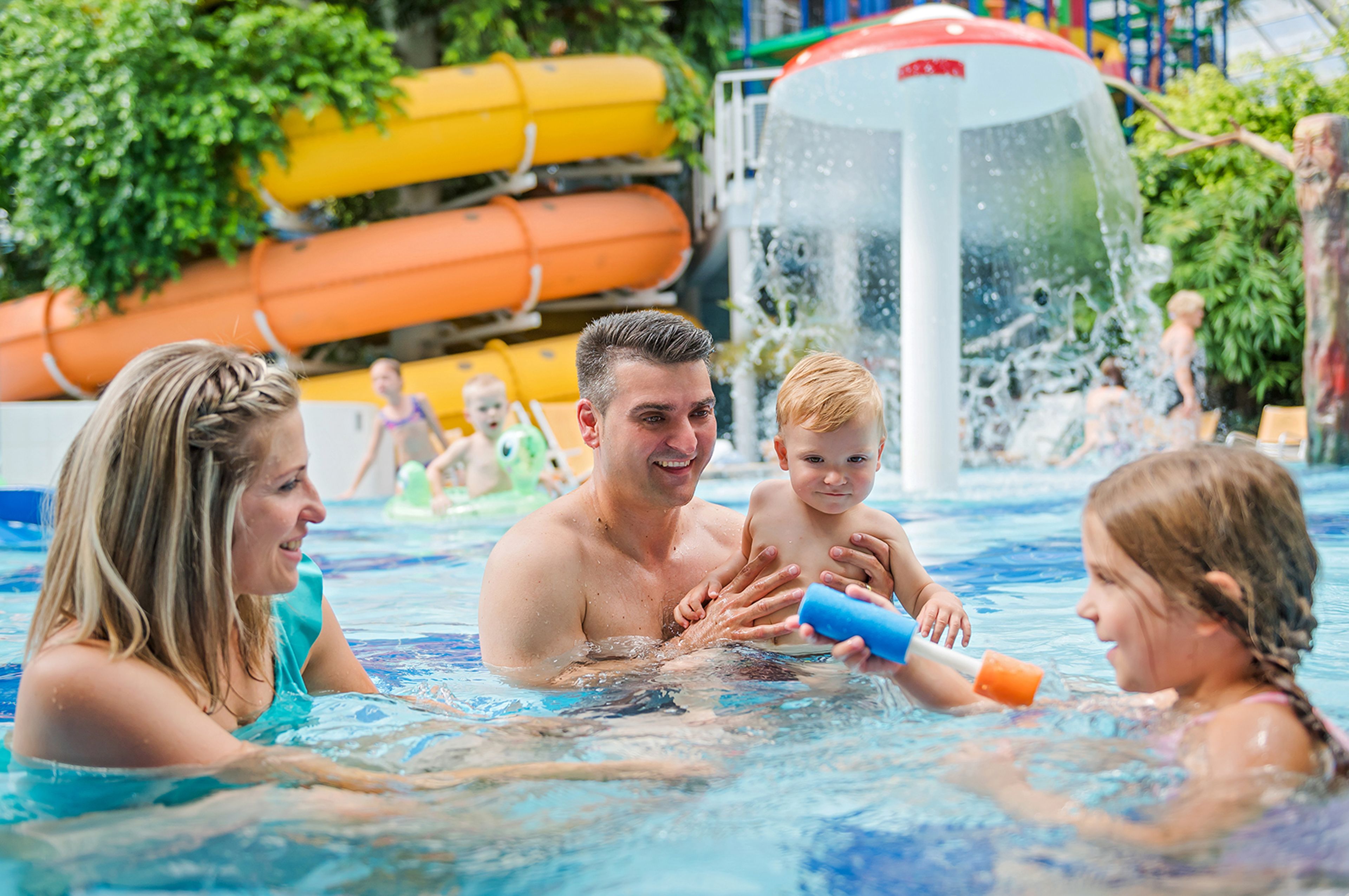 Una famiglia in piscina, con scivoli e gommoni sullo sfondo.