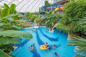 Une piscine intérieure dotée de toboggans et d’autres jeux d’eau, le tout entouré de plantes tropicales.