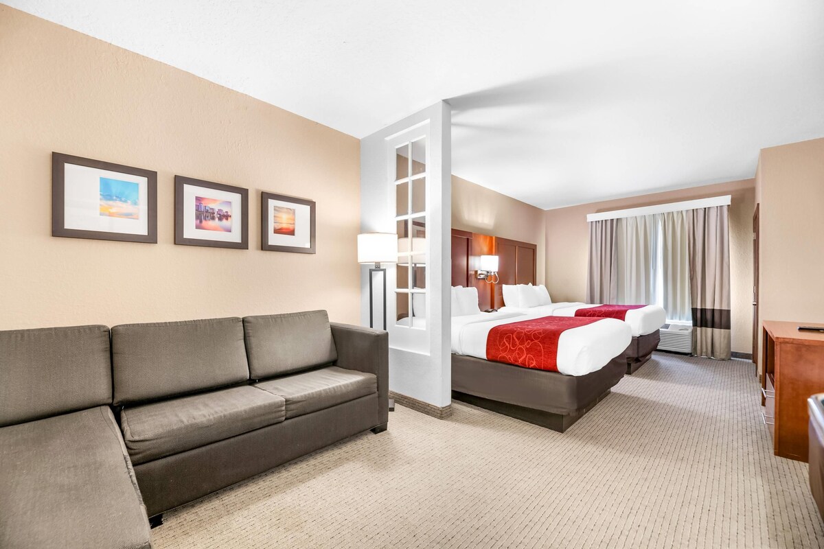 Une chambre d’hôtel avec un canapé, un lit avec une literie rouge, un bureau et une fenêtre avec des rideaux.