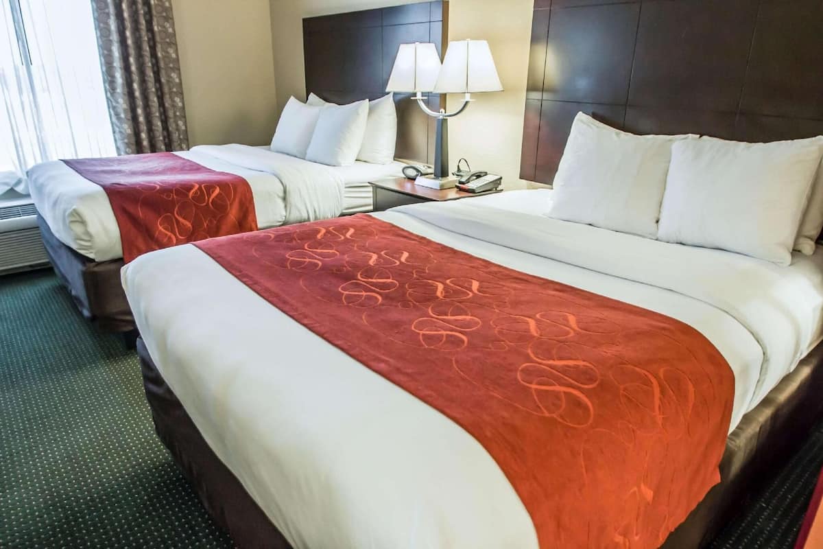 Een hotelkamer met twee bedden, een nachtkastje met een lamp en een raam met gordijnen.