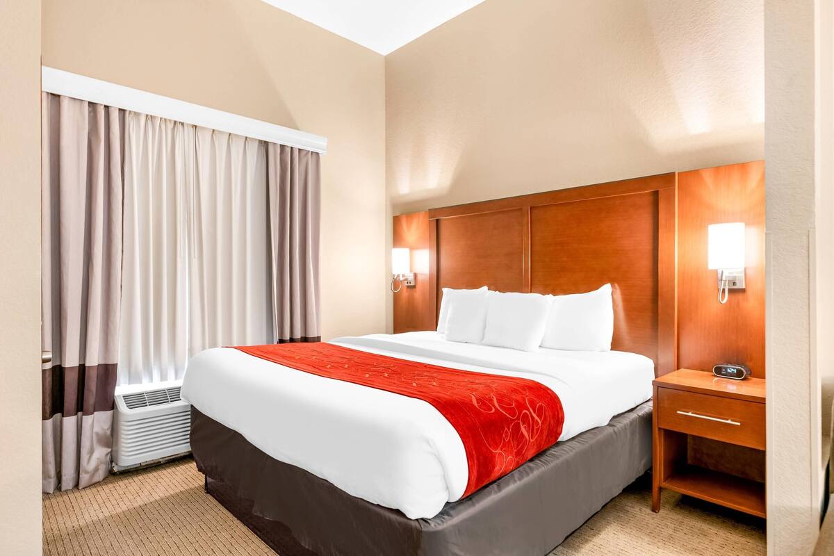 Een hotelkamer met een bed, nachtkastje, lamp en gordijnen.