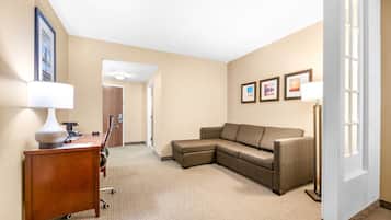 A hotel room with a wooden desk, a brown leather sofa, a standing lamp, and framed pictures on the wall.
