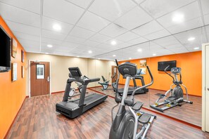 Een sportschool met diverse trainingsapparaten, een houten vloer en oranje wanden.