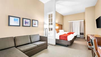 A hotel room with a sofa, a bed with a red blanket, a TV, and framed pictures on the wall.