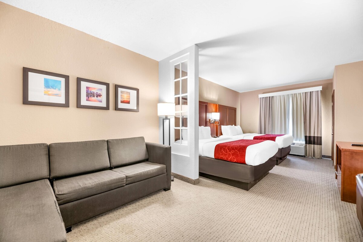 Een hotelkamer met een sofa, een bed met rode beddengoed, een bureau en een raam met gordijnen.