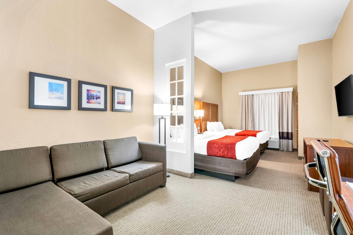 Een hotelkamer met een bank, een bed met een rode deken, een televisie en ingelijste foto's aan de muur.