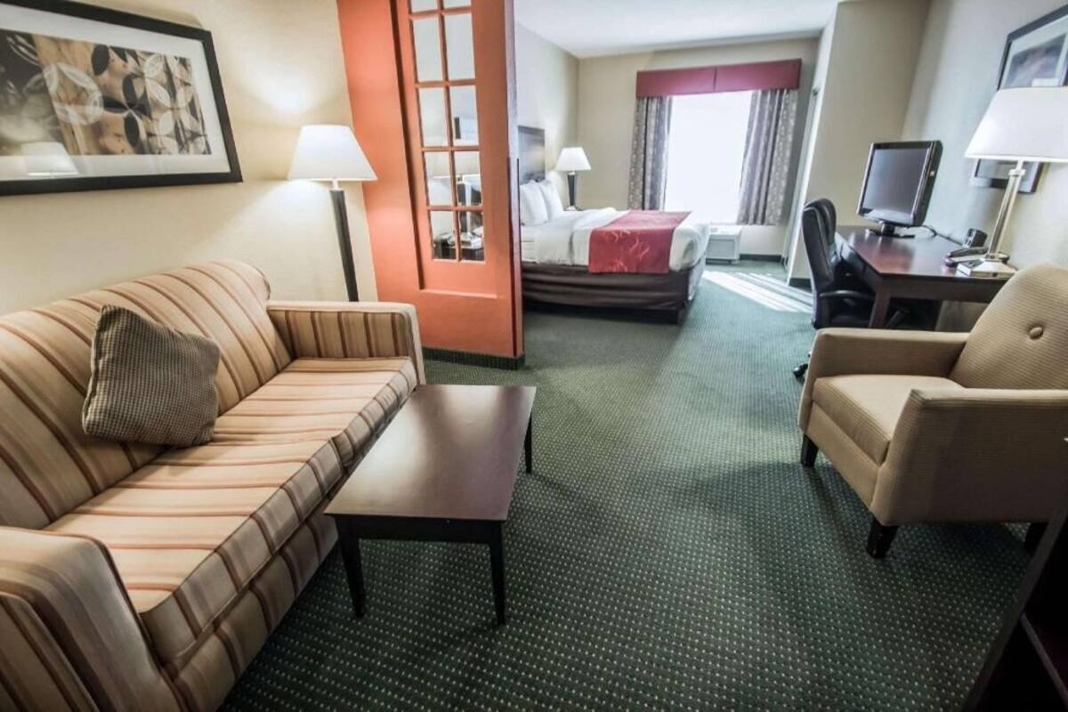 Een hotelkamer met een bank, een klein tafeltje, een bed, een bureau met een computer en een raam met gordijnen.