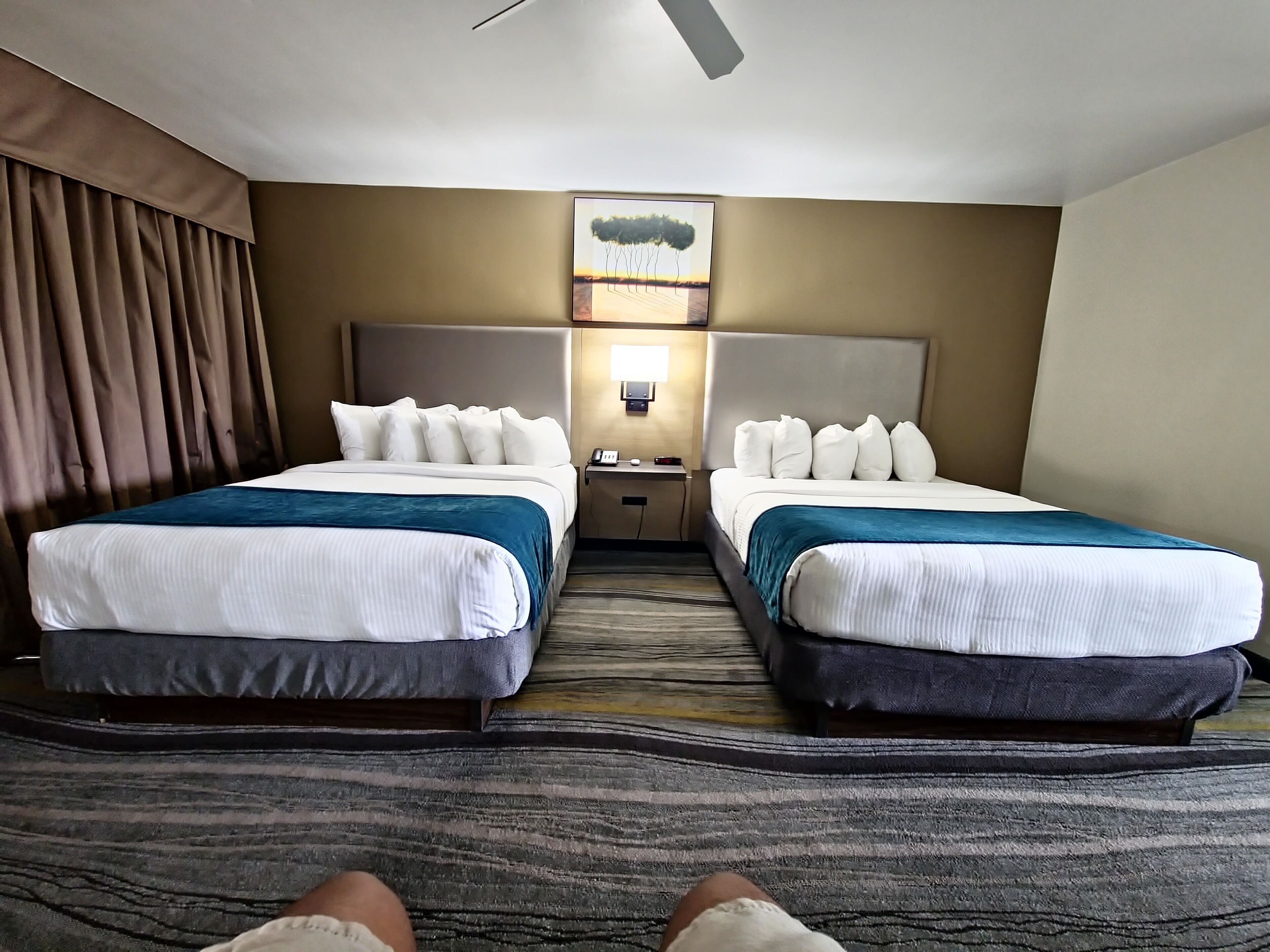A hotel room with two beds, a nightstand, a lamp, and a painting on the wall.