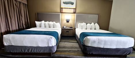 A hotel room with two beds, a nightstand, a lamp, and a painting on the wall.