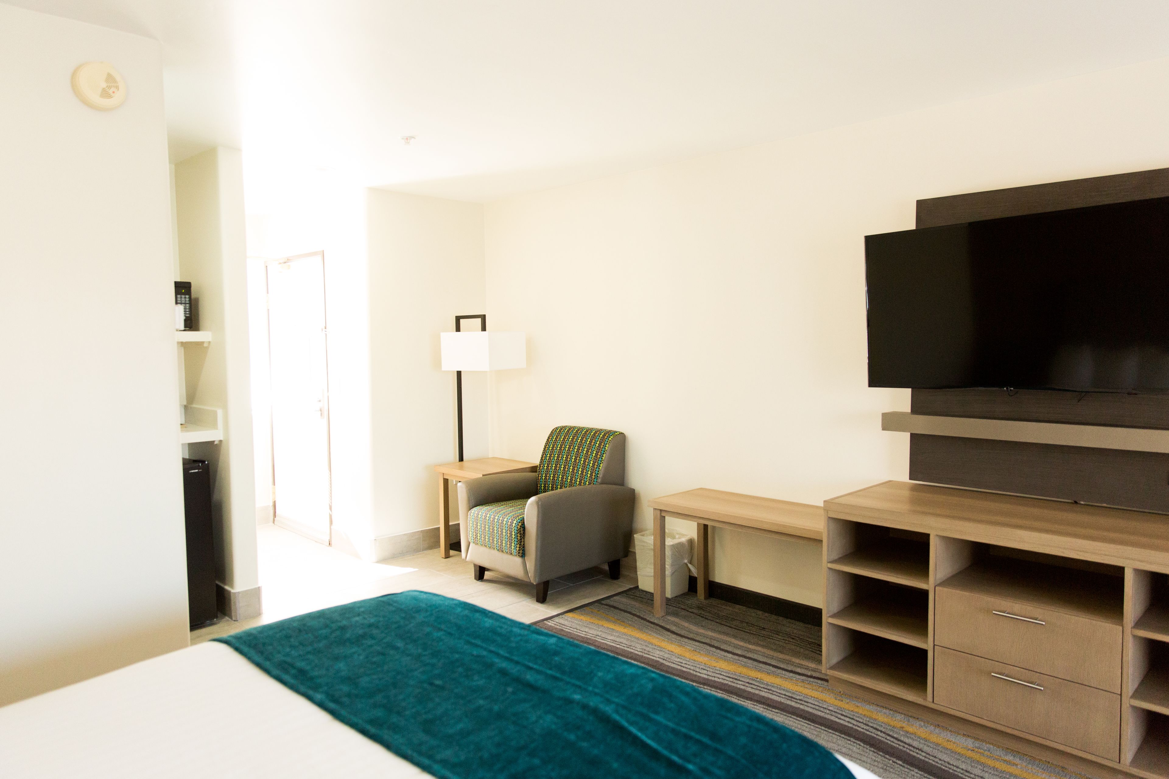 A hotel room with a bed, a desk, a chair, a TV, and a small shelf.