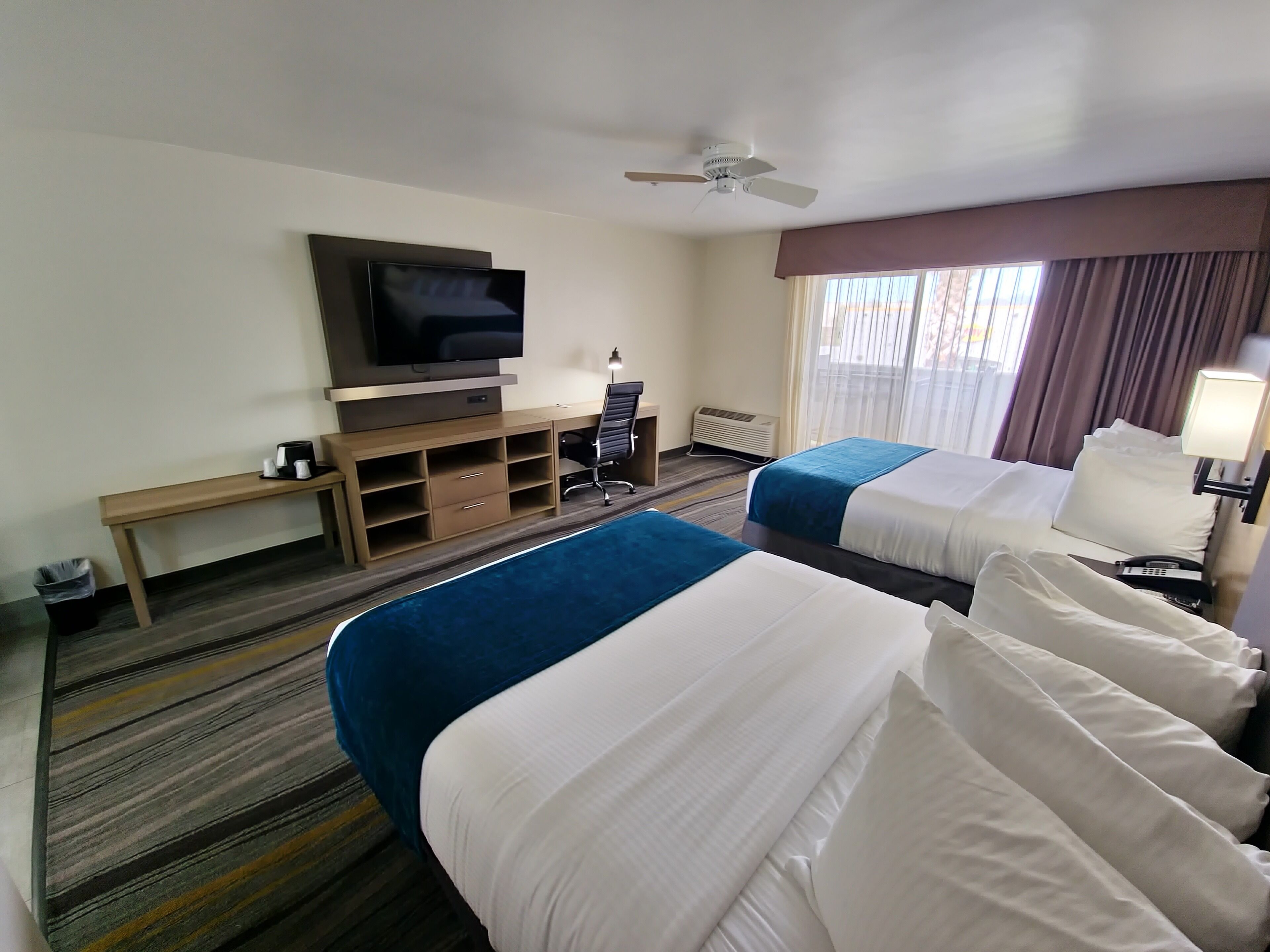 A hotel room with two beds, a TV, a desk, a chair, and a window with curtains.
