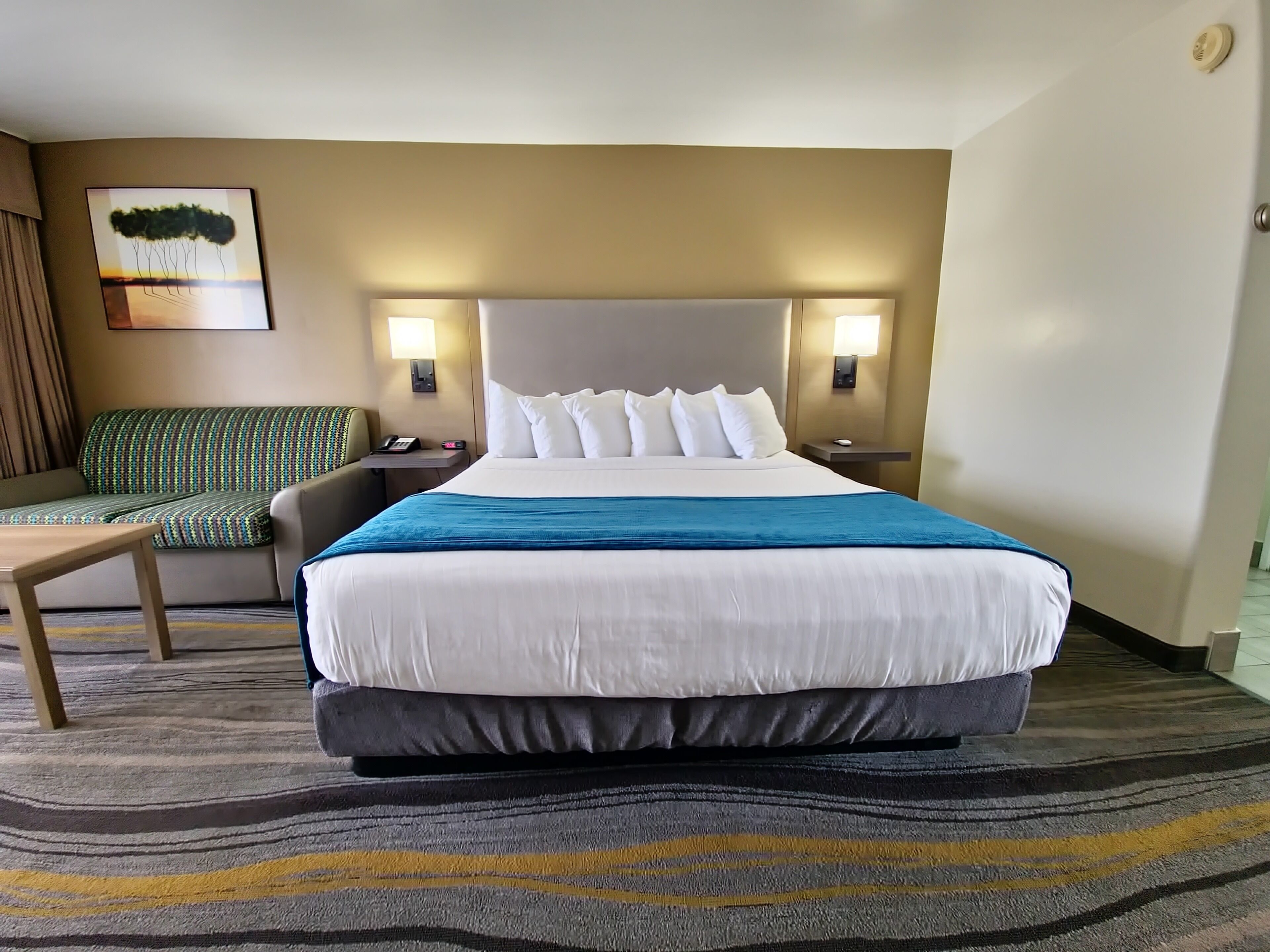 A hotel room with a large bed, a sofa, a desk, and a painting on the wall.