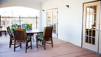 Un patio cubierto con mesa y sillas, una puerta y vista a la calle.