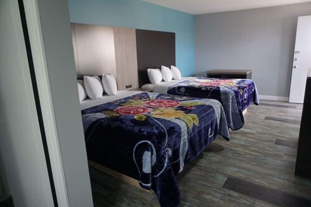 A hotel room with two beds, each with a floral bedspread, a wooden headboard, and a small bedside table.