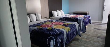 Habitación de hotel con dos camas, cada una con colcha estampada y cabecero de madera, junto a una mesita de noche.