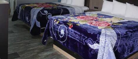 A hotel room with two beds, a wooden floor, and a blue accent wall.
