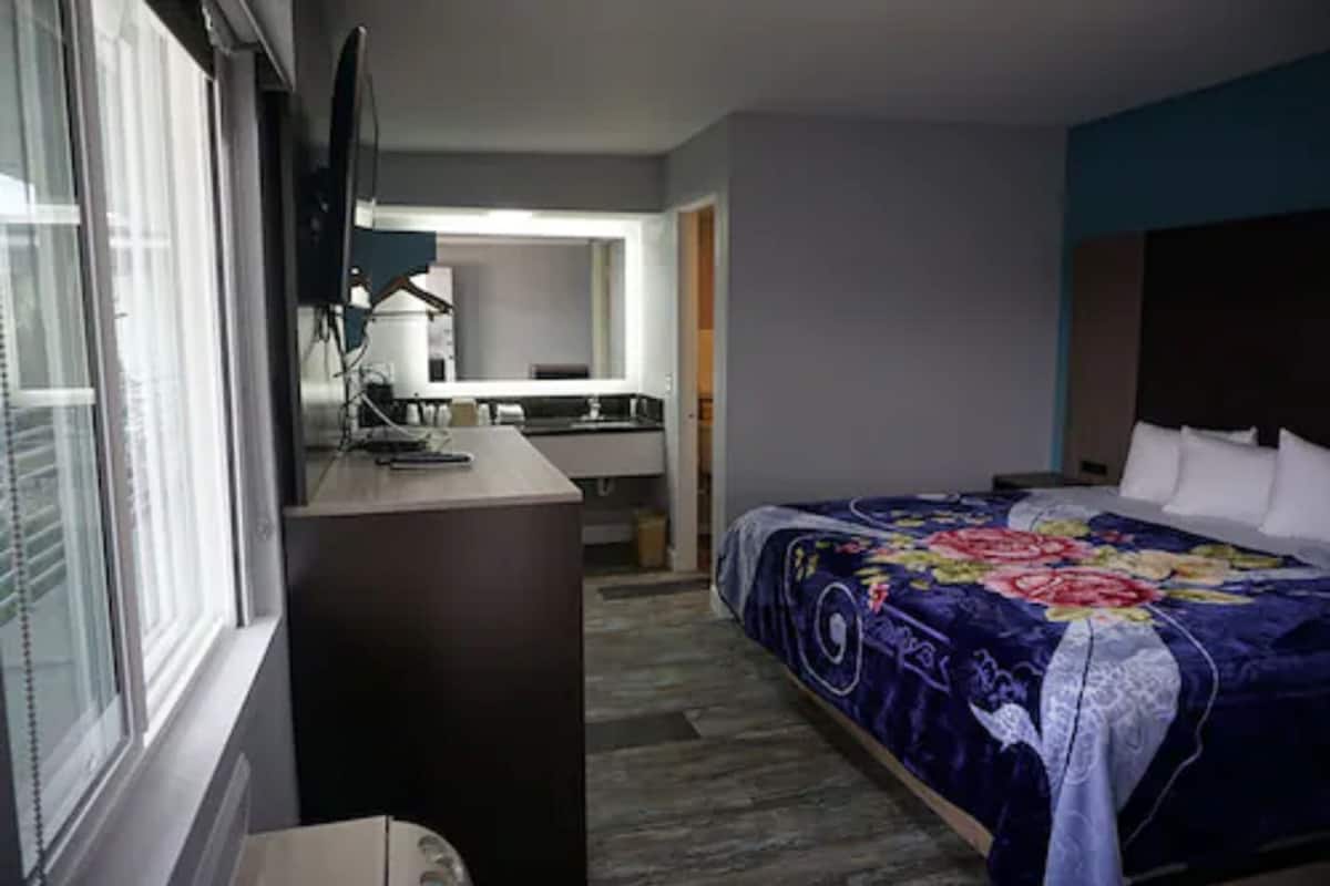 A hotel room with a bed, a desk, a chair, a television, and a bathroom visible through an open door.
