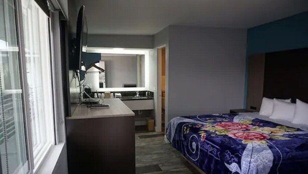 A hotel room with a bed, a desk, a chair, a television, and a bathroom visible through an open door.
