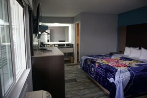A hotel room with a bed, a desk, a chair, a television, and a bathroom visible through an open door.