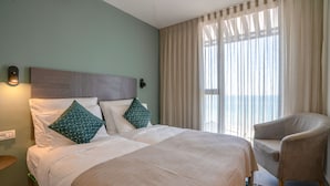 A hotel room with a large bed, two pillows, a chair, and a view of the outdoors through sheer curtains. - Roxon Sea Sand Bat Yam (Bat Yam)