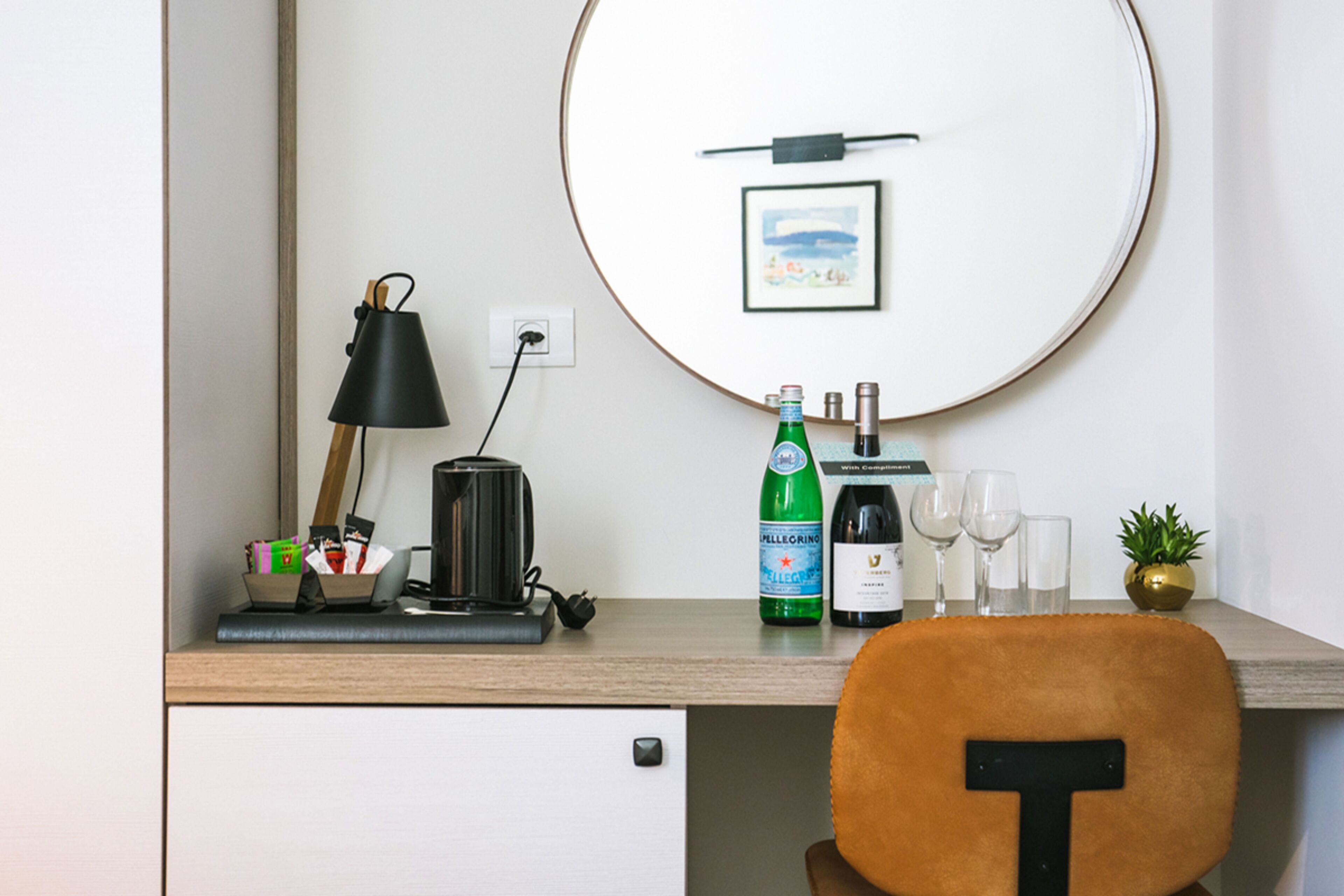 A desk with a lamp, a bottle of Pellegrino water, glasses, and a small plant.