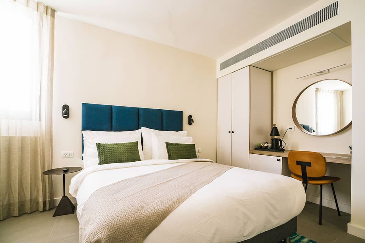 A hotel room with a bed, a desk, a chair, a round mirror, and a wardrobe.