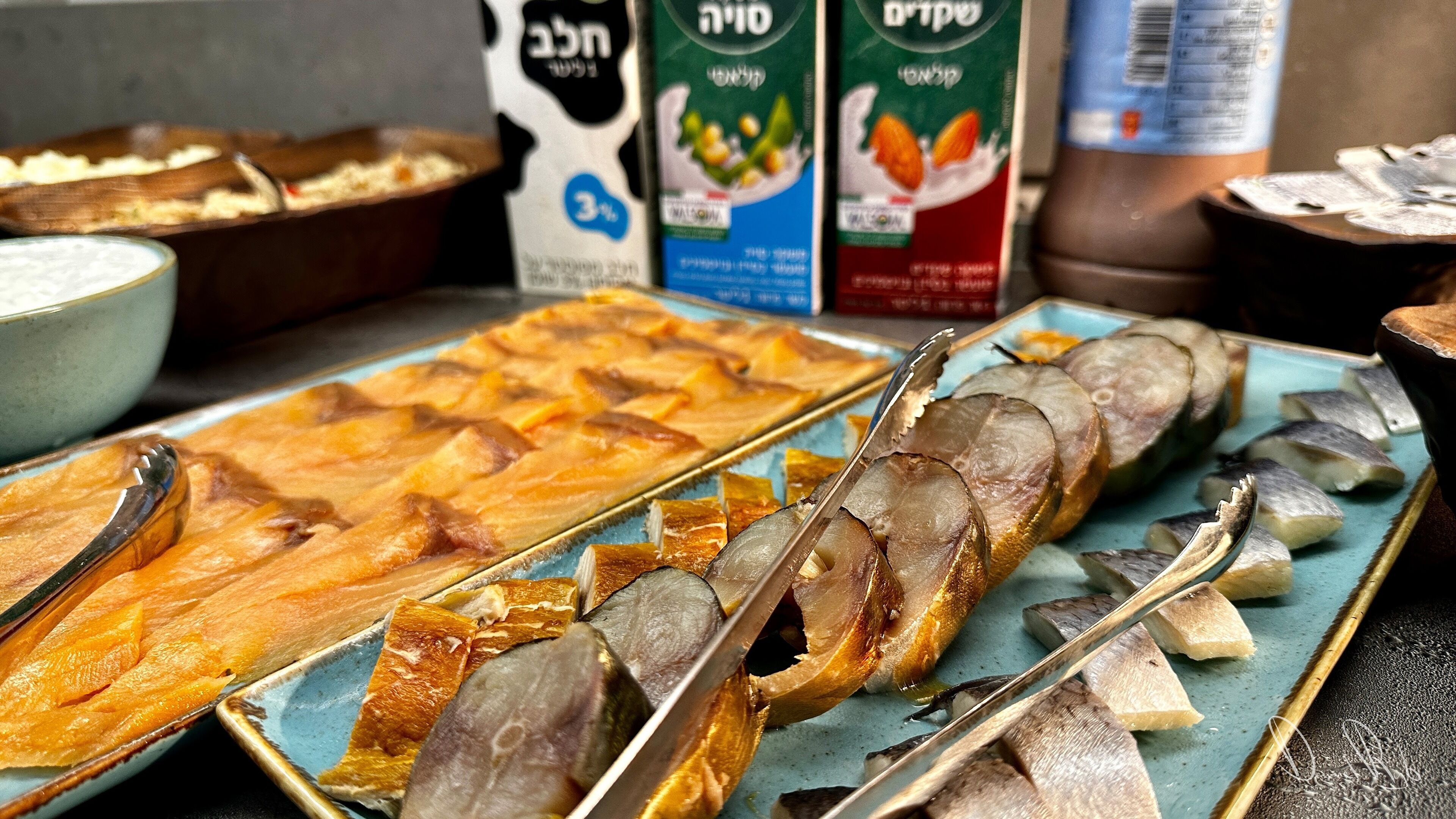 Variedad de mariscos en una bandeja, incluyendo pescado y posiblemente otros mariscos, con un tazón de sopa y cartones de leche al fondo.