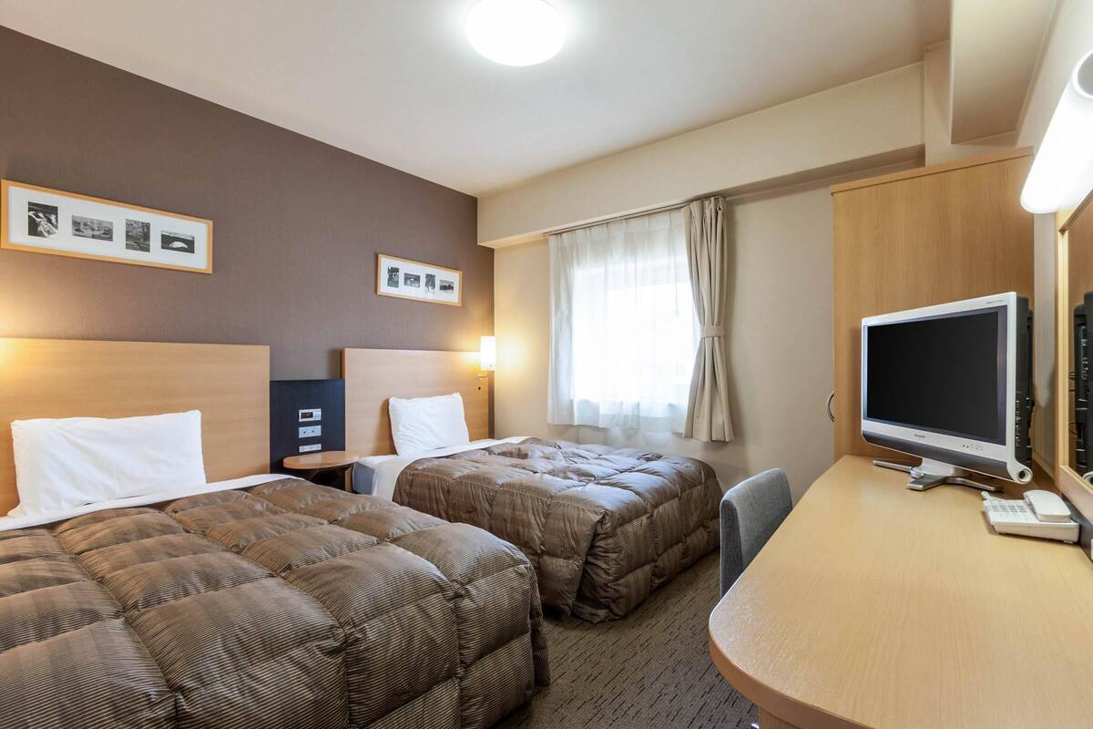 A hotel room with two beds, a desk with a computer, and a TV.