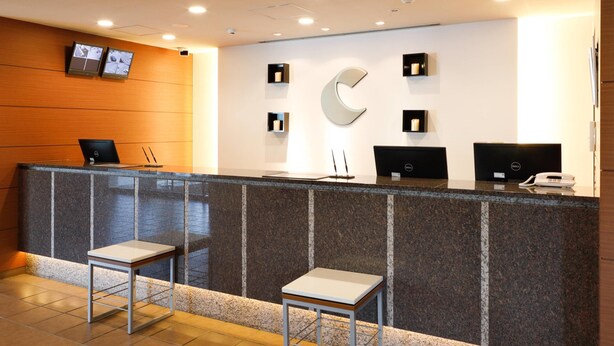 A reception area with a marble counter, two chairs, a large C-shaped wall decoration, and a Dell computer on the counter. - Comfort Hotel Obihiro (Obihiro)