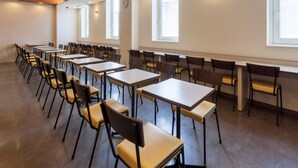 A conference room with rows of tables and chairs, large windows, and a wooden ceiling. - Comfort Hotel Obihiro (Obihiro)