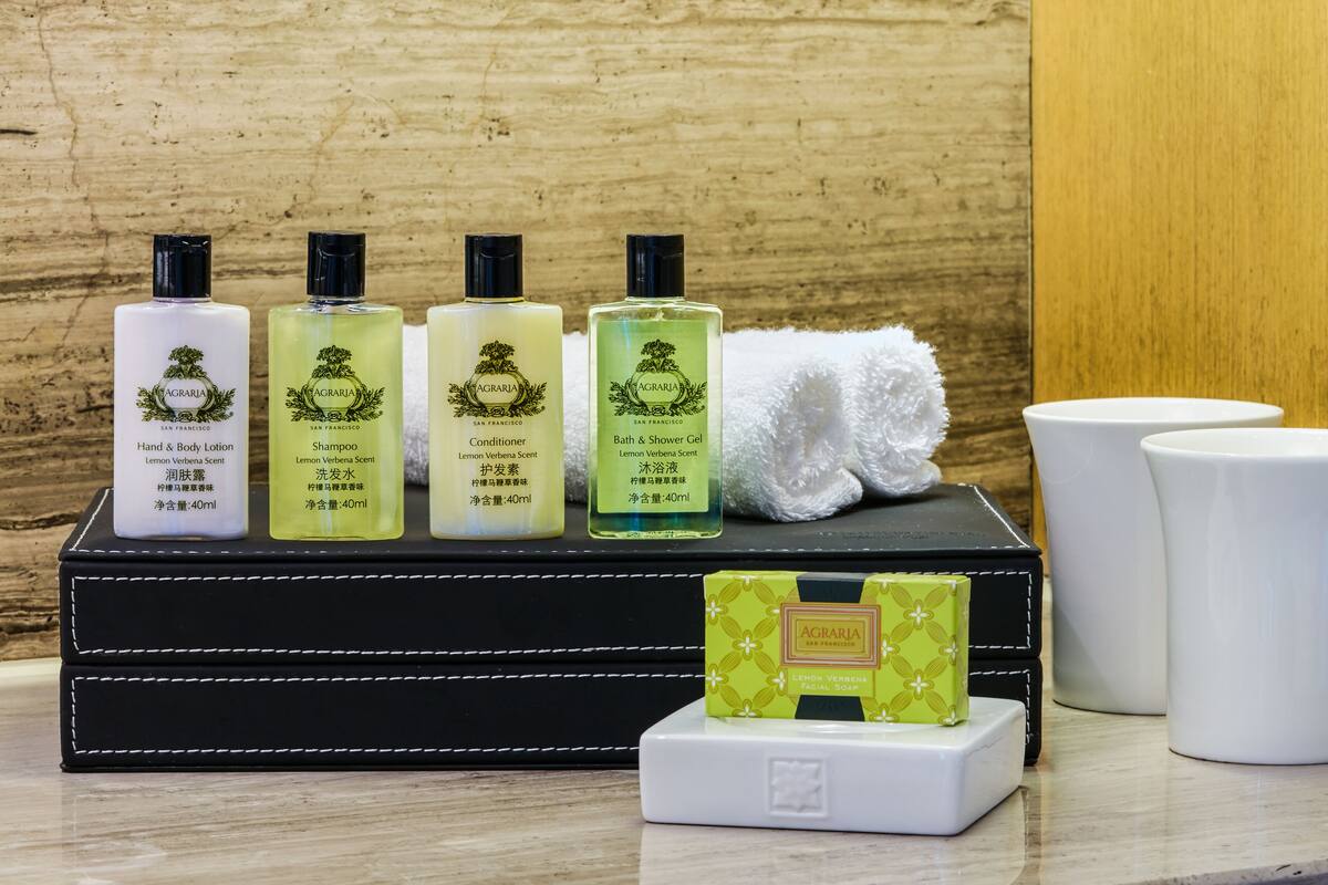 A set of toiletries including hand and body lotion, shampoo, conditioner, and bath & shower gel, along with a facial soap and two white cups, all arranged on a black tray.