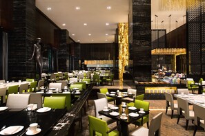 A spacious restaurant with multiple dining tables and chairs, a central bar area, and a decorative sculpture. - InterContinental Shanghai Jing’ An by IHG (Shanghai)