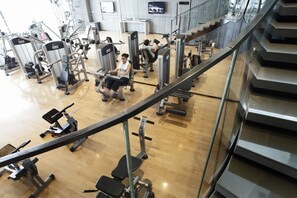 A gym with various exercise machines, a wooden floor, and a staircase.