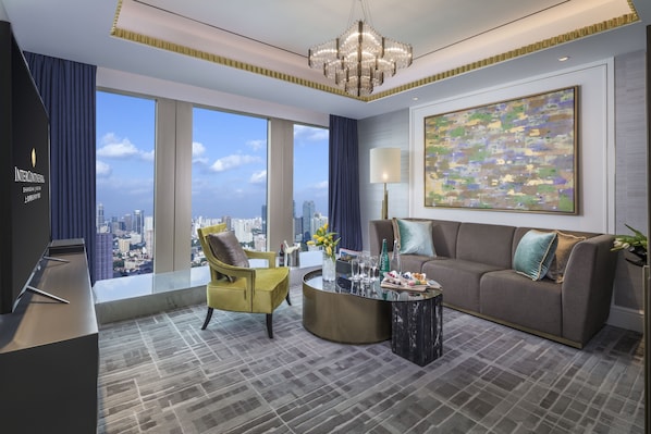 Una habitación de hotel moderna con vistas a la ciudad, un ventanal grande, un sofá, un sillón amarillo, una mesita de centro redonda y una araña.