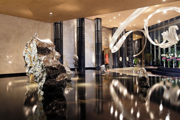 A modern lobby with reflective floors, large decorative columns, and abstract wall art.
