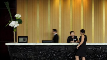 A reception desk with a marble top, a framed informational sign, and a floral arrangement.