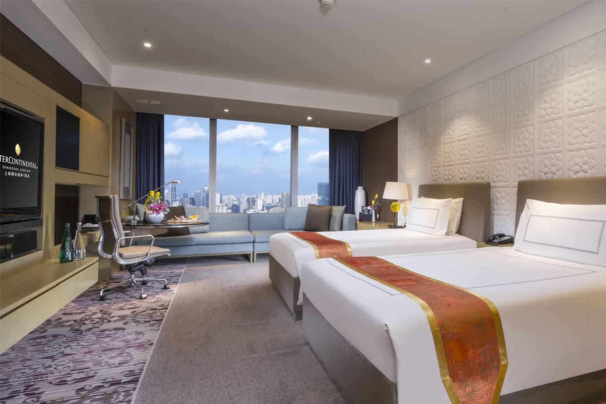 A hotel room with two beds, a sofa, a TV, and a city view.