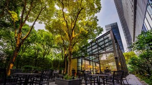 An outdoor cafe with tables and chairs, surrounded by trees and a modern building in the background. - InterContinental Shanghai Jing’ An by IHG (Shanghai)