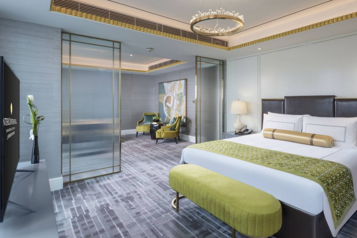 A modern hotel room with a large bed, a bench, a desk, and a chair.
